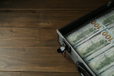 Metal case full of dollar banknotes on wooden table, space for text