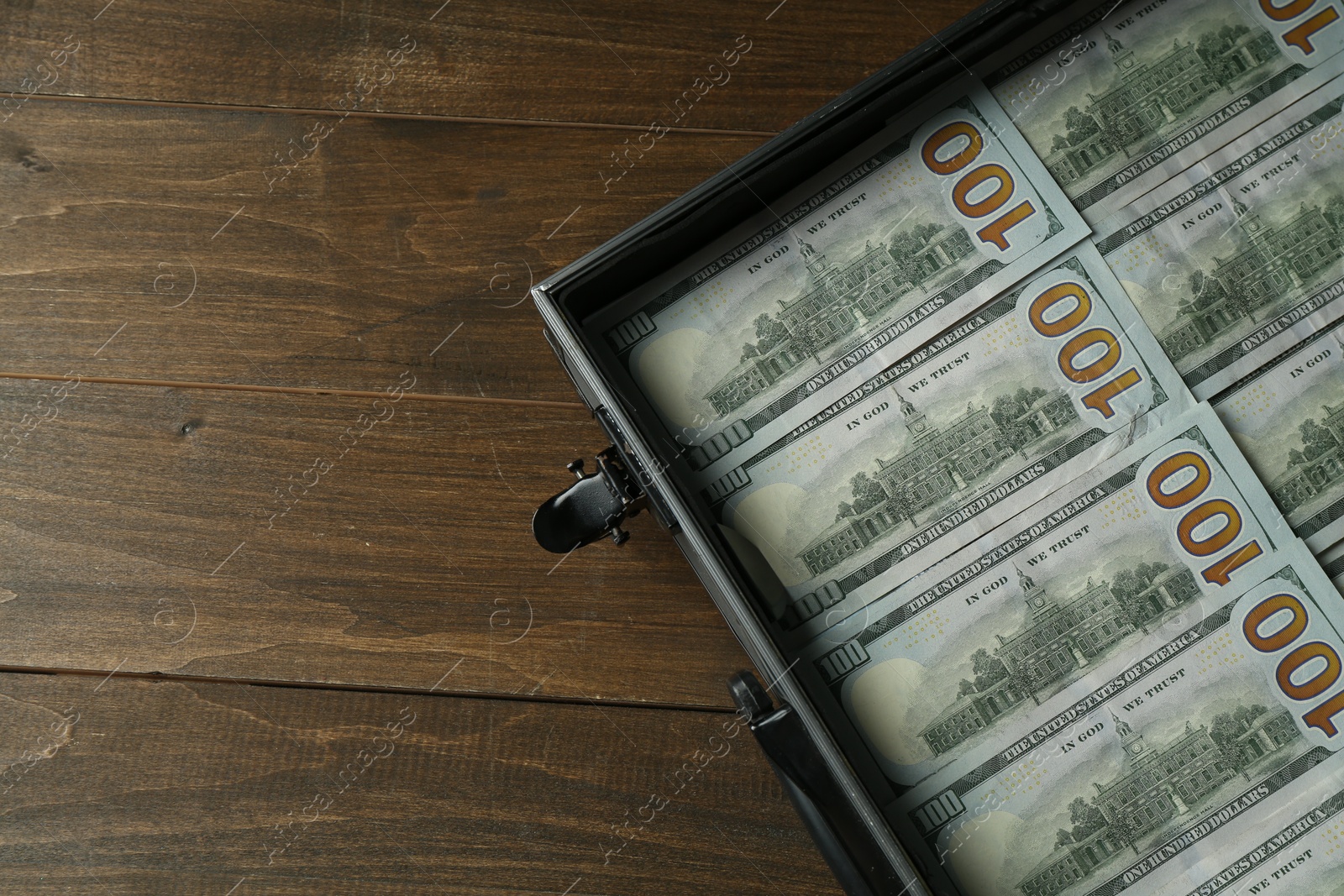 Photo of Metal case full of dollar banknotes on wooden table, top view. Space for text