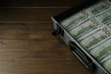 Metal case full of dollar banknotes on wooden table, space for text