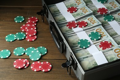 Photo of Metal case full of dollar banknotes and casino chips on wooden table