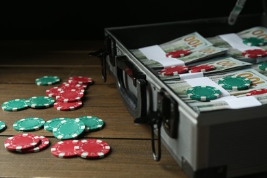 Metal case full of dollar banknotes and casino chips on wooden table, closeup