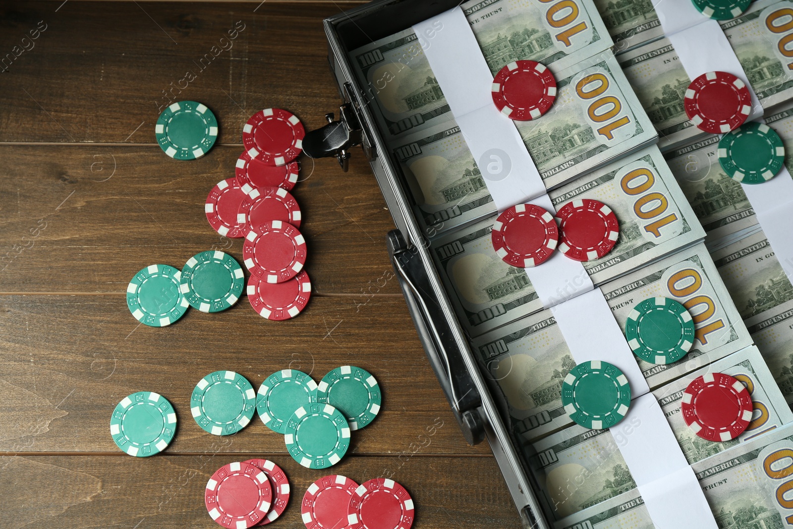 Photo of Metal case full of dollar banknotes and casino chips on wooden table, above view