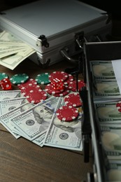 Photo of Metal cases full of dollar banknotes and casino chips on wooden table