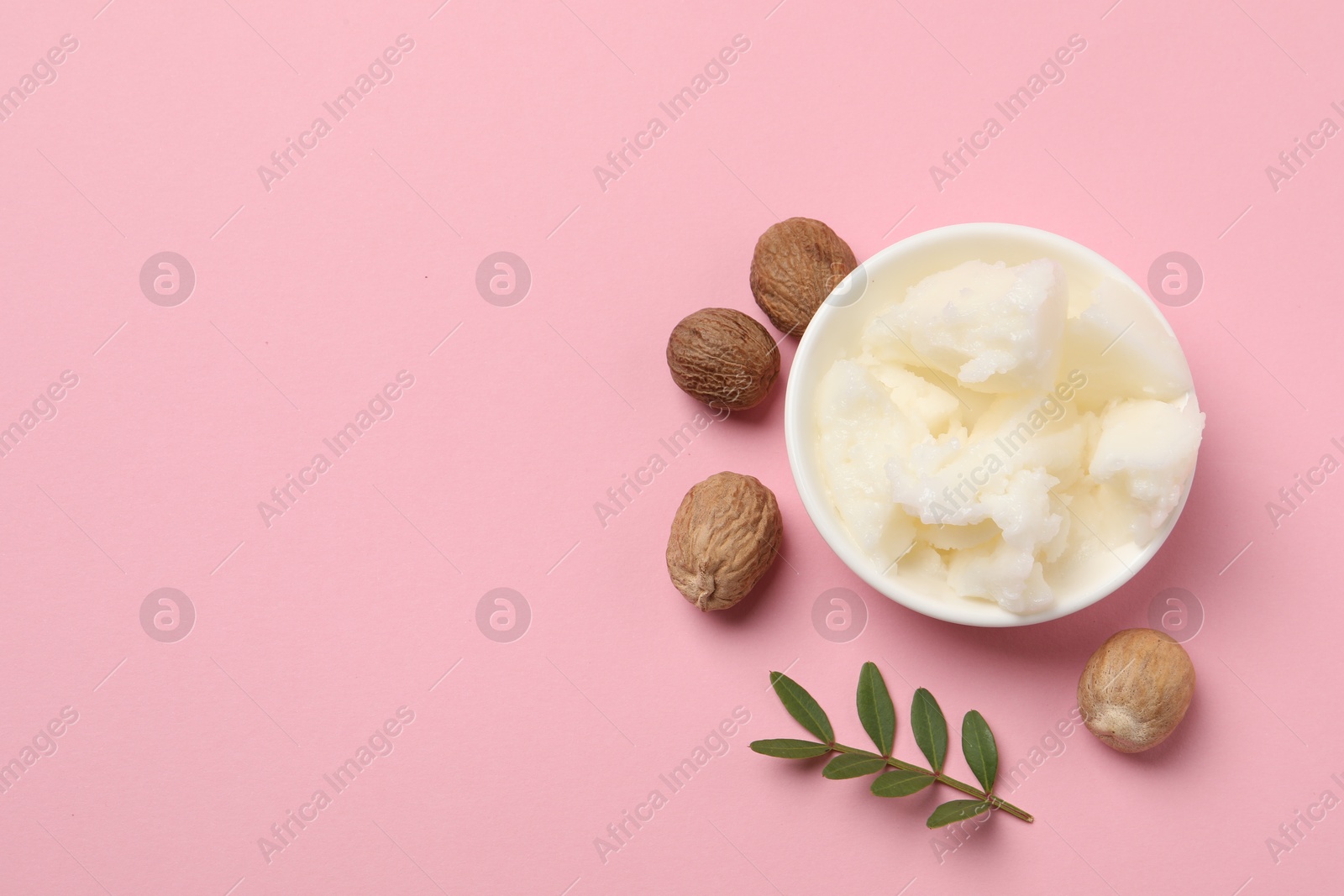 Photo of Natural shea butter in bowl, nuts and green twig on pink background, top view. Space for text