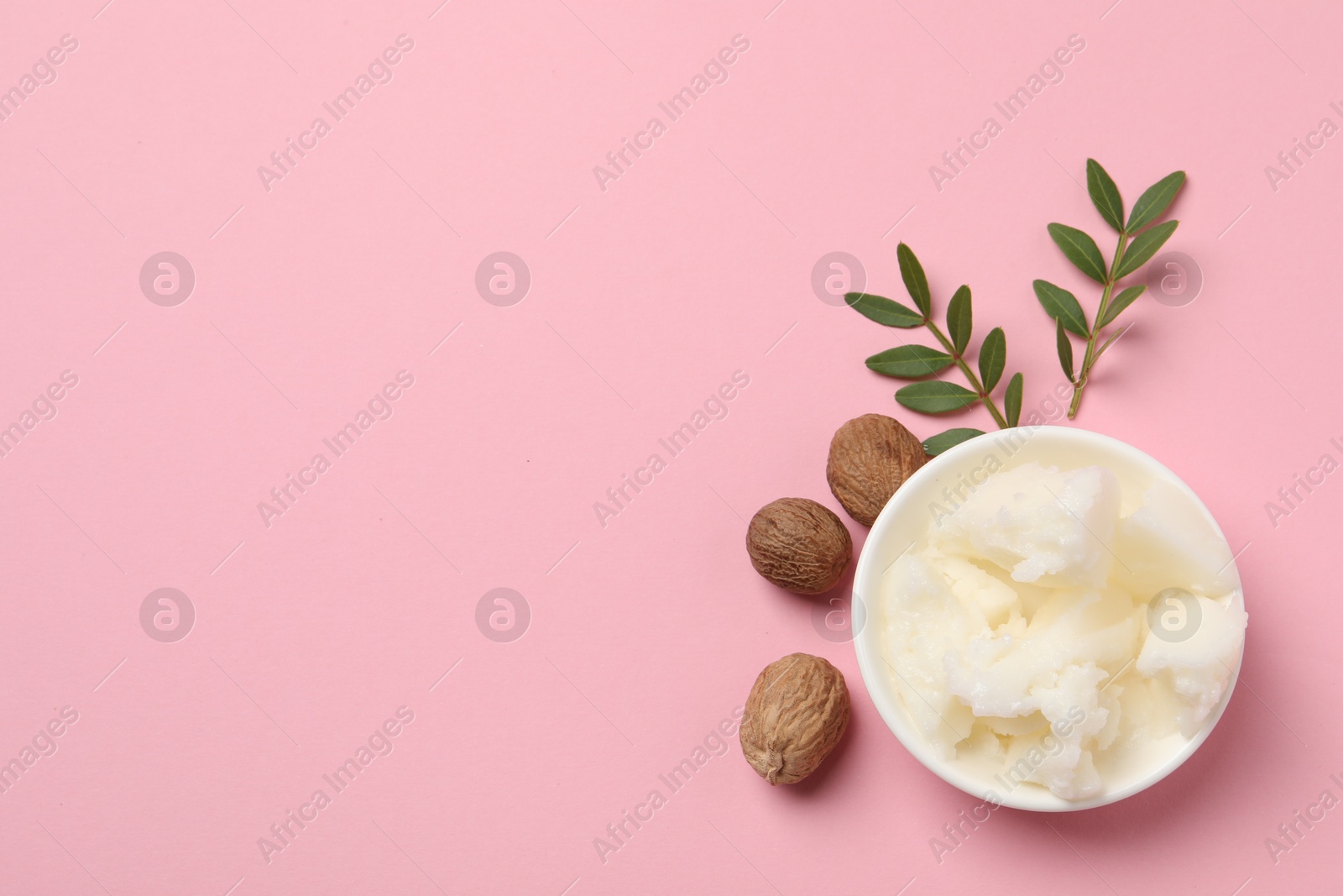 Photo of Natural shea butter in bowl, nuts and green leaves on pink background, top view. Space for text