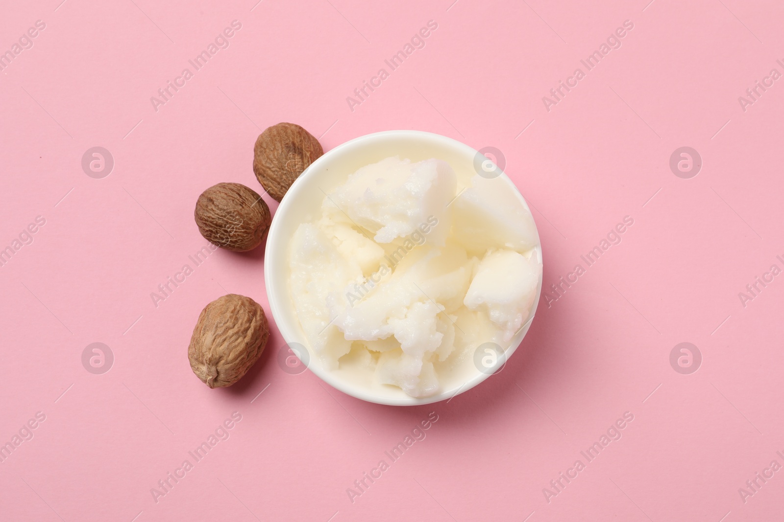 Photo of Natural shea butter in bowl and nuts on pink background, top view