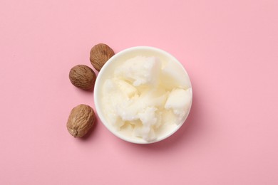 Natural shea butter in bowl and nuts on pink background, top view