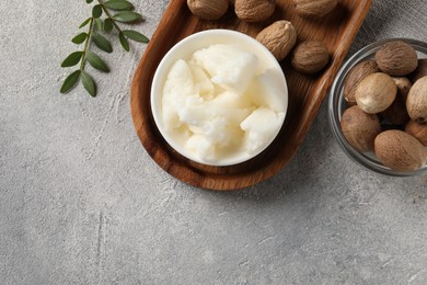 Natural shea butter in bowl, nuts and green leaves on grey table, top view. Space for text