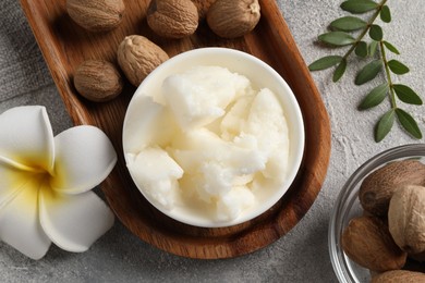 Photo of Natural shea butter in bowl, nuts, green leaves and plumeria flower on grey table, top view