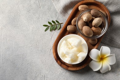 Photo of Natural shea butter in bowl, nuts, green twig and plumeria flower on grey table, top view. Space for text