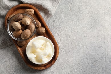 Natural shea butter in bowl and nuts on grey table, top view. Space for text