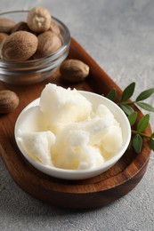 Natural shea butter in bowl, nuts, green leaves and plumeria flower on grey table