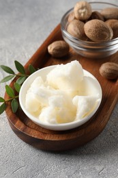 Photo of Natural shea butter in bowl, nuts, green leaves and plumeria flower on grey table