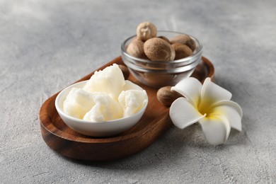 Photo of Natural shea butter in bowl, nuts and plumeria flower on grey table