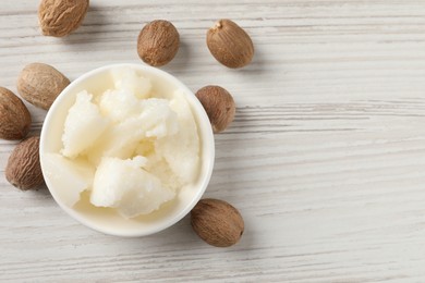 Photo of Natural shea butter in bowl and nuts on wooden table, top view. Space for text