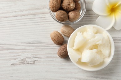 Photo of Natural shea butter in bowl, nuts and plumeria flower on wooden table, top view. Space for text