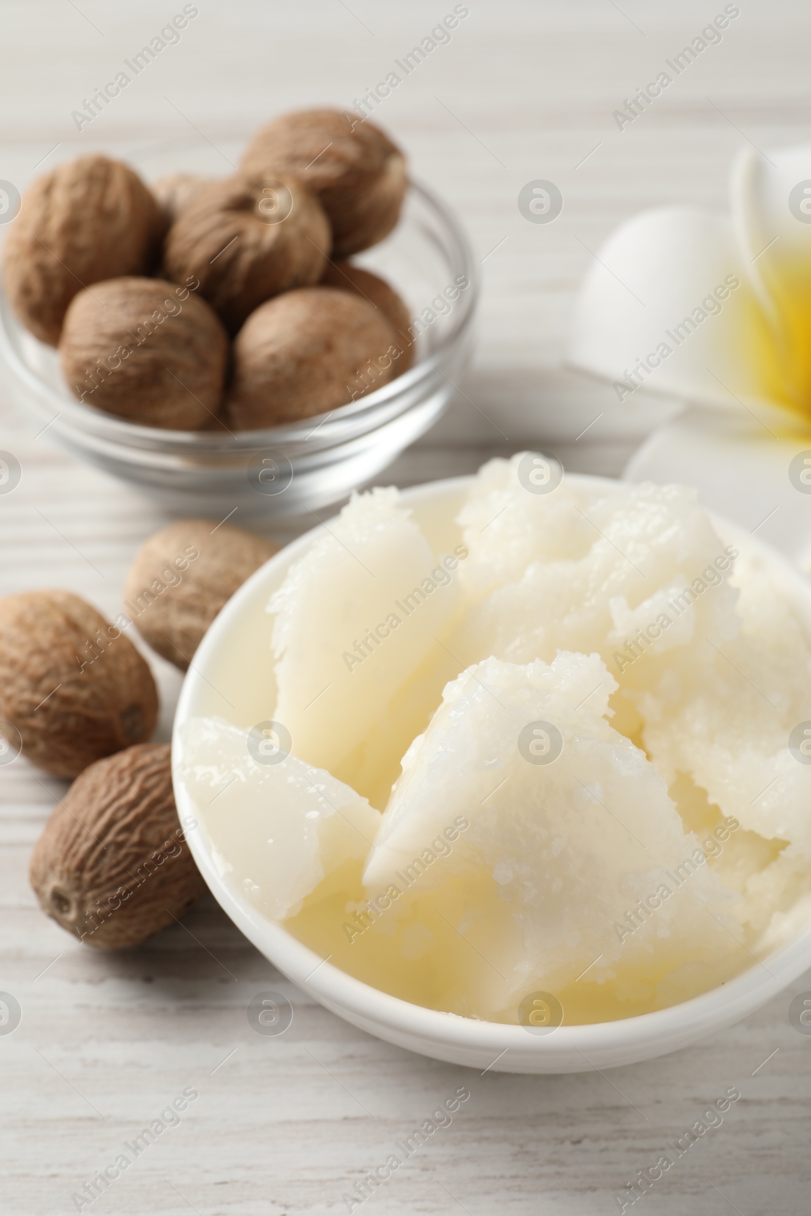 Photo of Natural shea butter in bowl, nuts and plumeria flower on wooden table