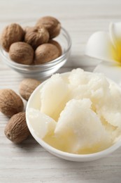 Natural shea butter in bowl, nuts and plumeria flower on wooden table