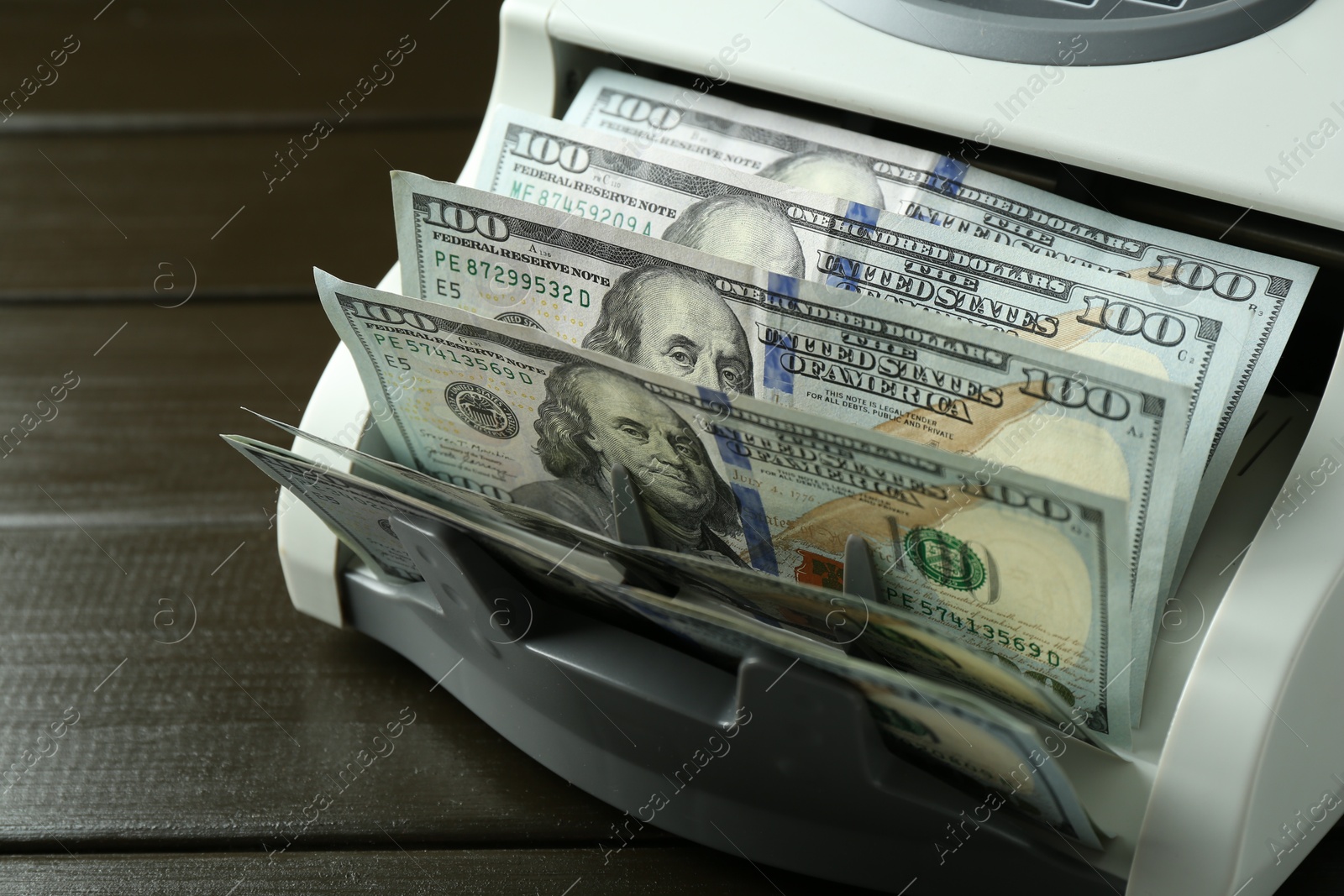 Photo of Money counter machine with dollar banknotes on wooden table, closeup