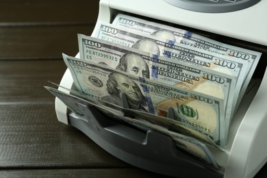 Money counter machine with dollar banknotes on wooden table, closeup