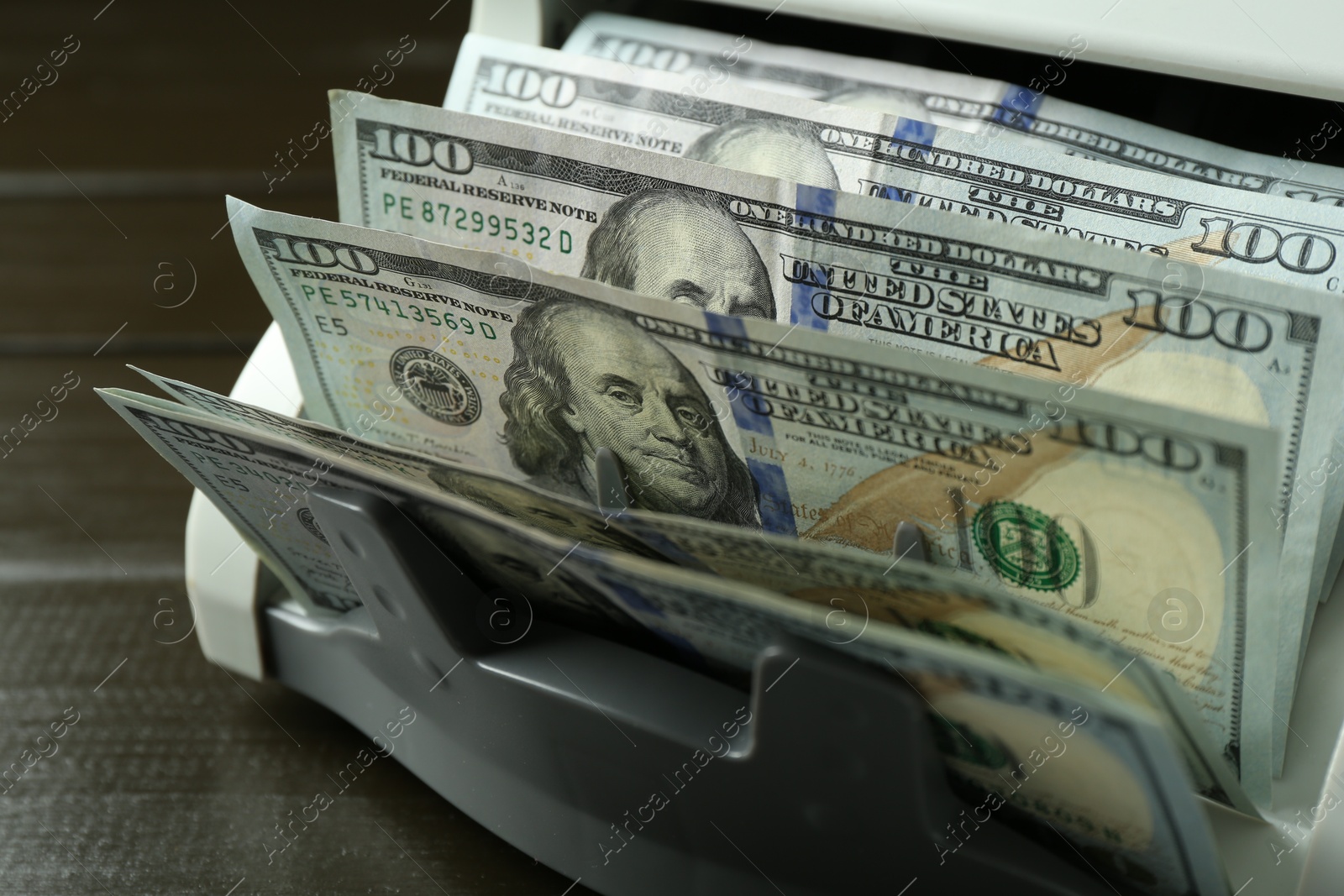 Photo of Money counter machine with dollar banknotes on wooden table, closeup