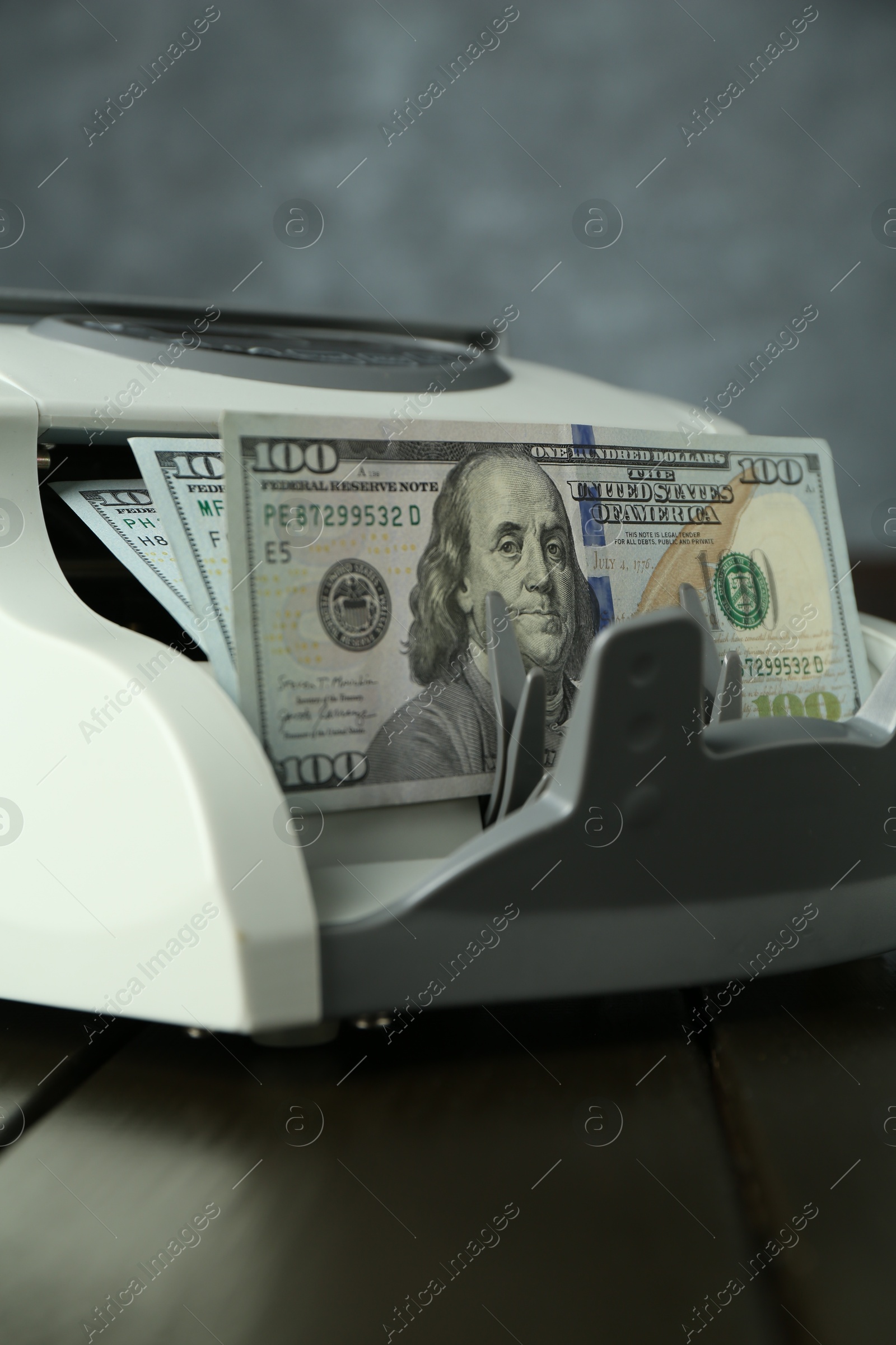 Photo of Money counter machine with dollar banknotes on wooden table