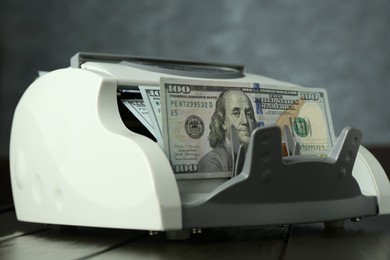 Photo of Money counter machine with dollar banknotes on wooden table