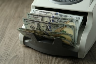 Photo of Money counter machine with dollar banknotes on wooden table, closeup