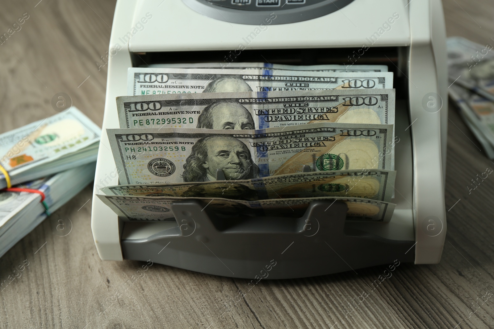 Photo of Money counter machine with dollar banknotes on wooden table