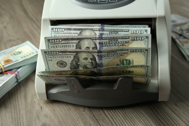 Money counter machine with dollar banknotes on wooden table