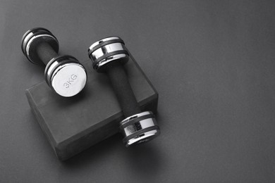 Two dumbbells and yoga block on black background, above view. Space for text