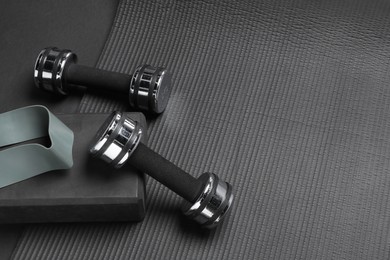 Dumbbells, yoga block, mat and fitness elastic band on black background, above view. Space for text