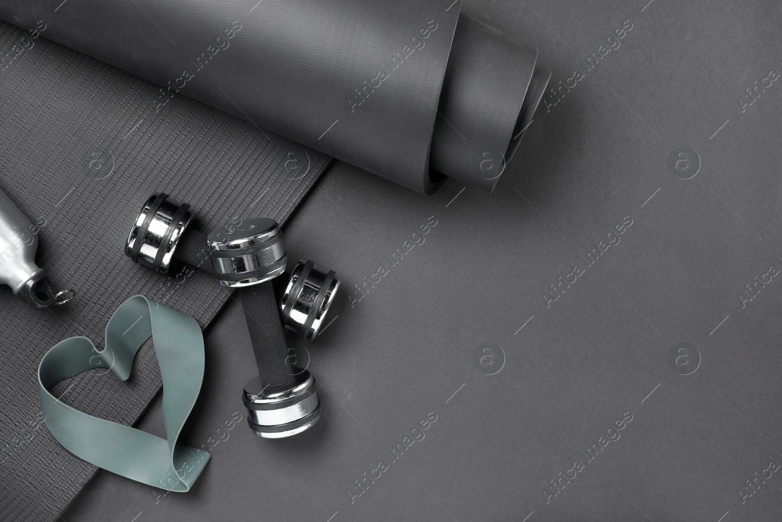 Photo of Dumbbells, yoga mat, thermo bottle and fitness elastic band on black background, flat lay. Space for text