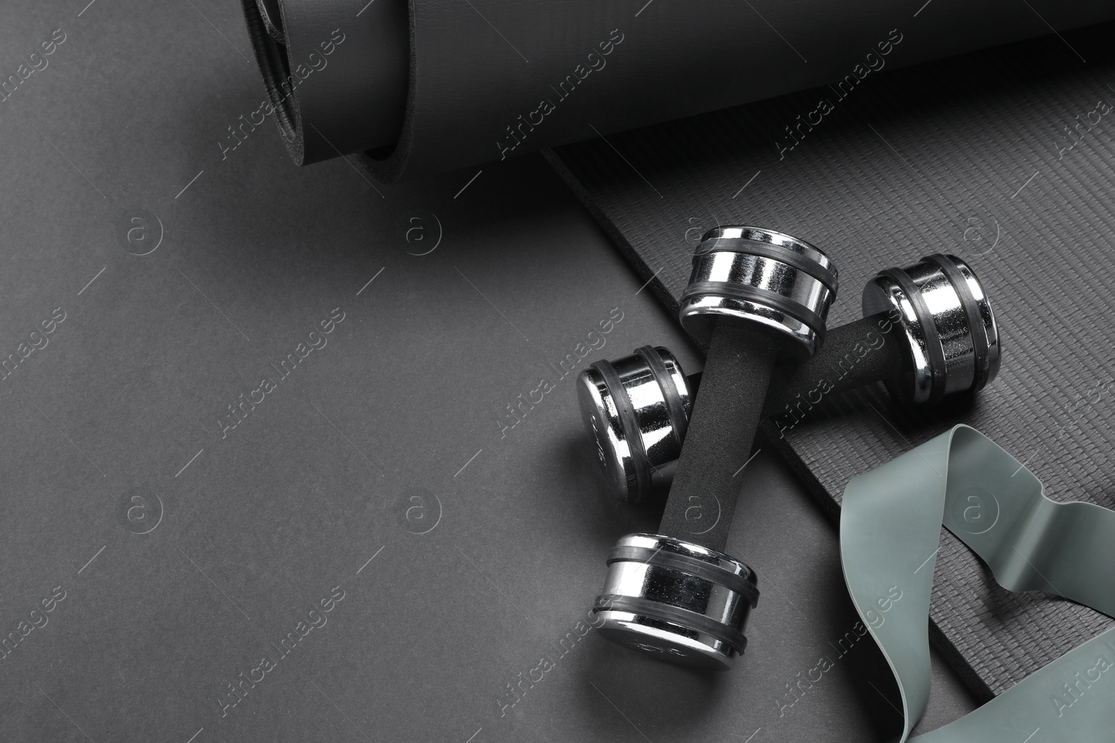 Photo of Dumbbells, yoga mat and fitness elastic band on black background, above view. Space for text