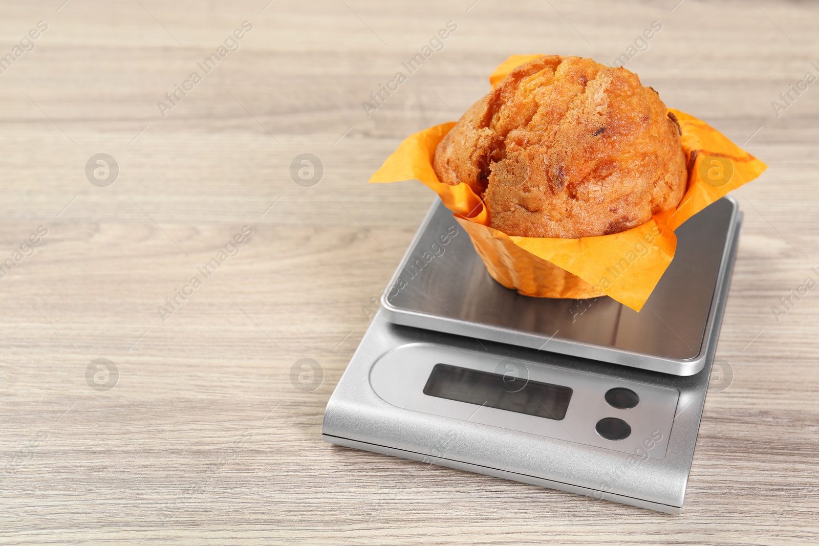 Photo of Kitchen scale with muffin on light wooden table, closeup. Space for text