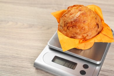 Photo of Kitchen scale with muffin on light wooden table, closeup. Space for text