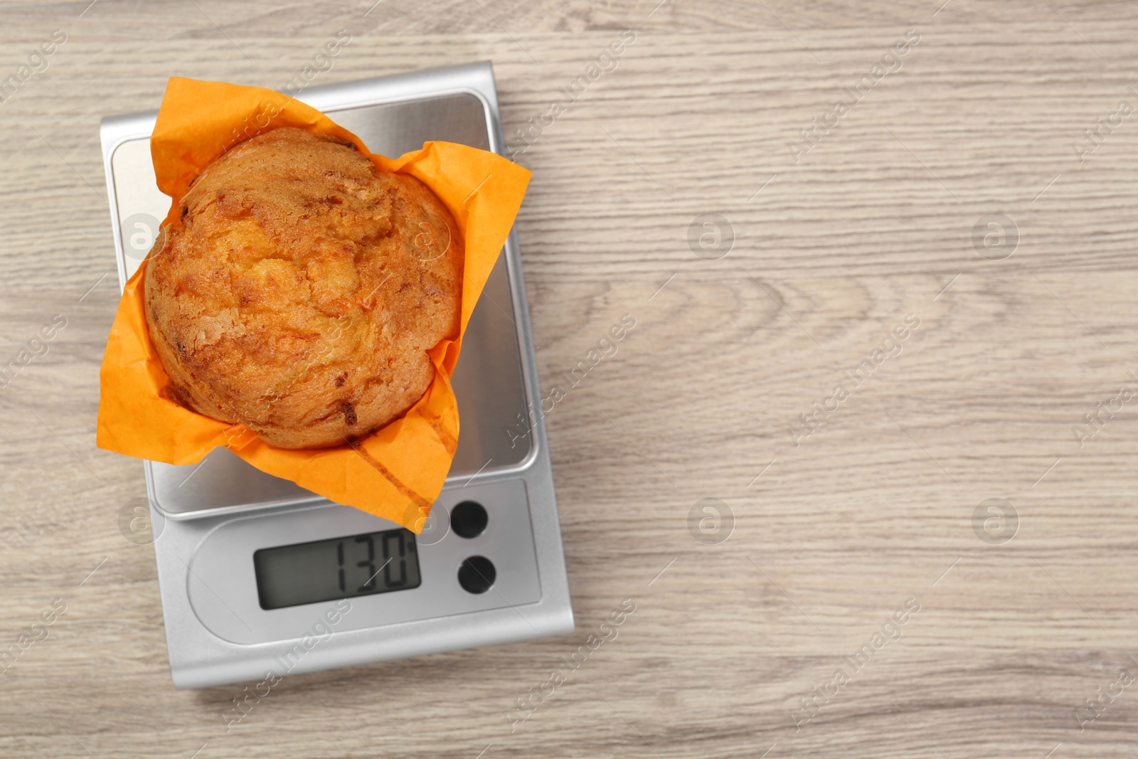 Photo of Kitchen scale with muffin on light wooden table, top view. Space for text