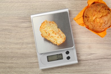 Photo of Kitchen scale with piece of muffin on light wooden table, flat lay