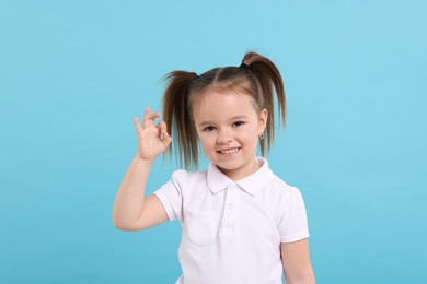 Photo of Portrait of happy little girl showing OK gesture on light blue background