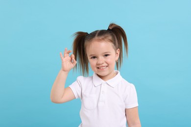 Portrait of happy little girl showing OK gesture on light blue background