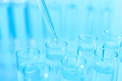 Photo of Dripping liquid from pipette into test tube on light blue background, closeup