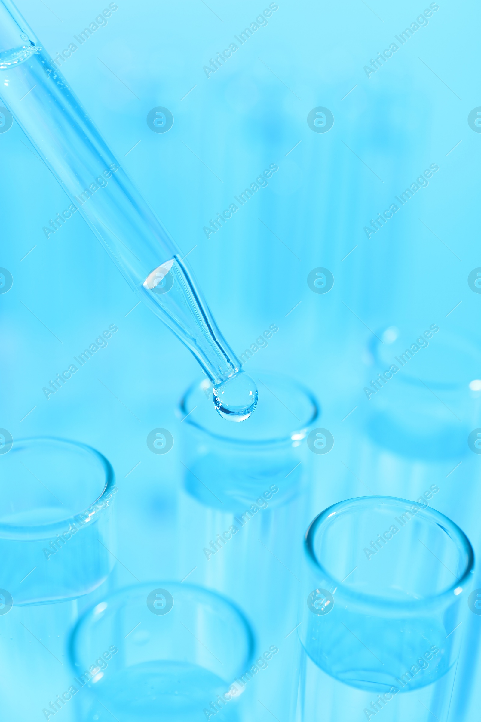 Photo of Dripping liquid from pipette into test tube on light blue background, closeup