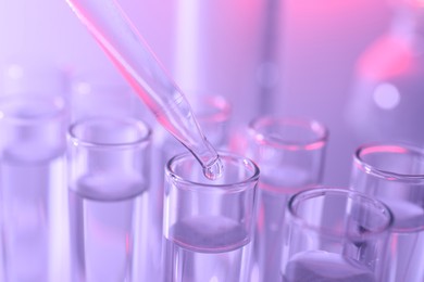 Photo of Dripping liquid from pipette into test tube on violet background, closeup