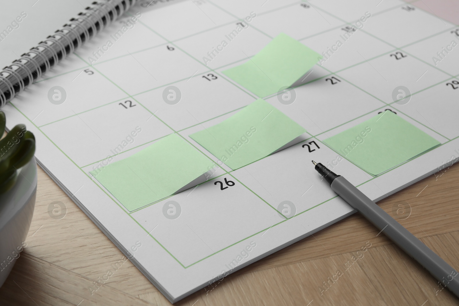 Photo of Timetable. Calendar page with green sticky notes and pen on wooden table, closeup