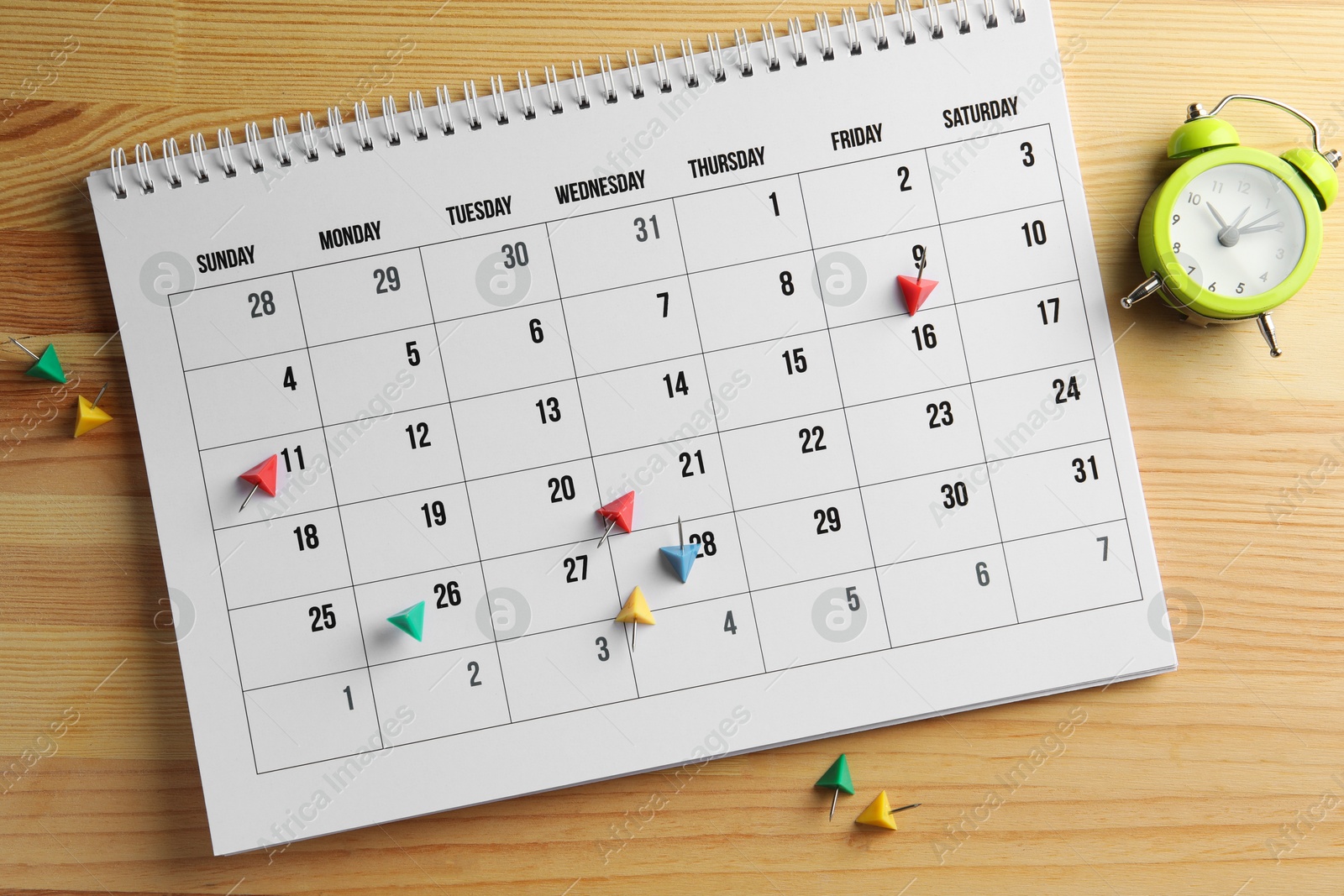 Photo of Timetable. Calendar, drawing pins and alarm clock on wooden table, top view