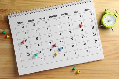 Timetable. Calendar, drawing pins and alarm clock on wooden table, top view