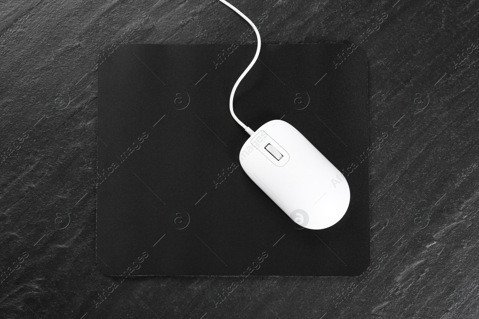 Photo of White wired mouse and mousepad on black textured table, top view