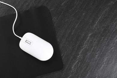 Photo of White wired mouse and mousepad on black textured table, top view