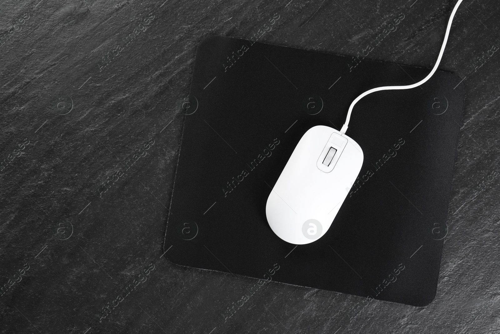 Photo of White wired mouse and mousepad on black textured table, top view