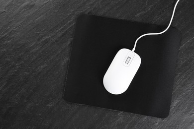 White wired mouse and mousepad on black textured table, top view